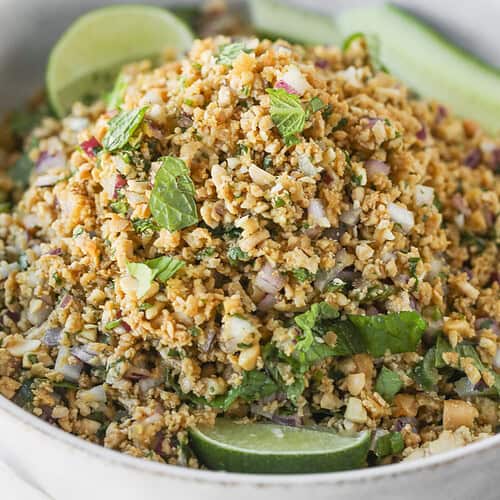 Vegan Thai Larb Lettuce Wraps 8 A Close-Up Of A Bowl Filled With A Chopped Salad Made From Cauliflower, Herbs, Onions, And Other Vegetables—Perfect For Vegan Thai Larb Lettuce Wraps—Garnished With Fresh Mint And Lime Wedges.