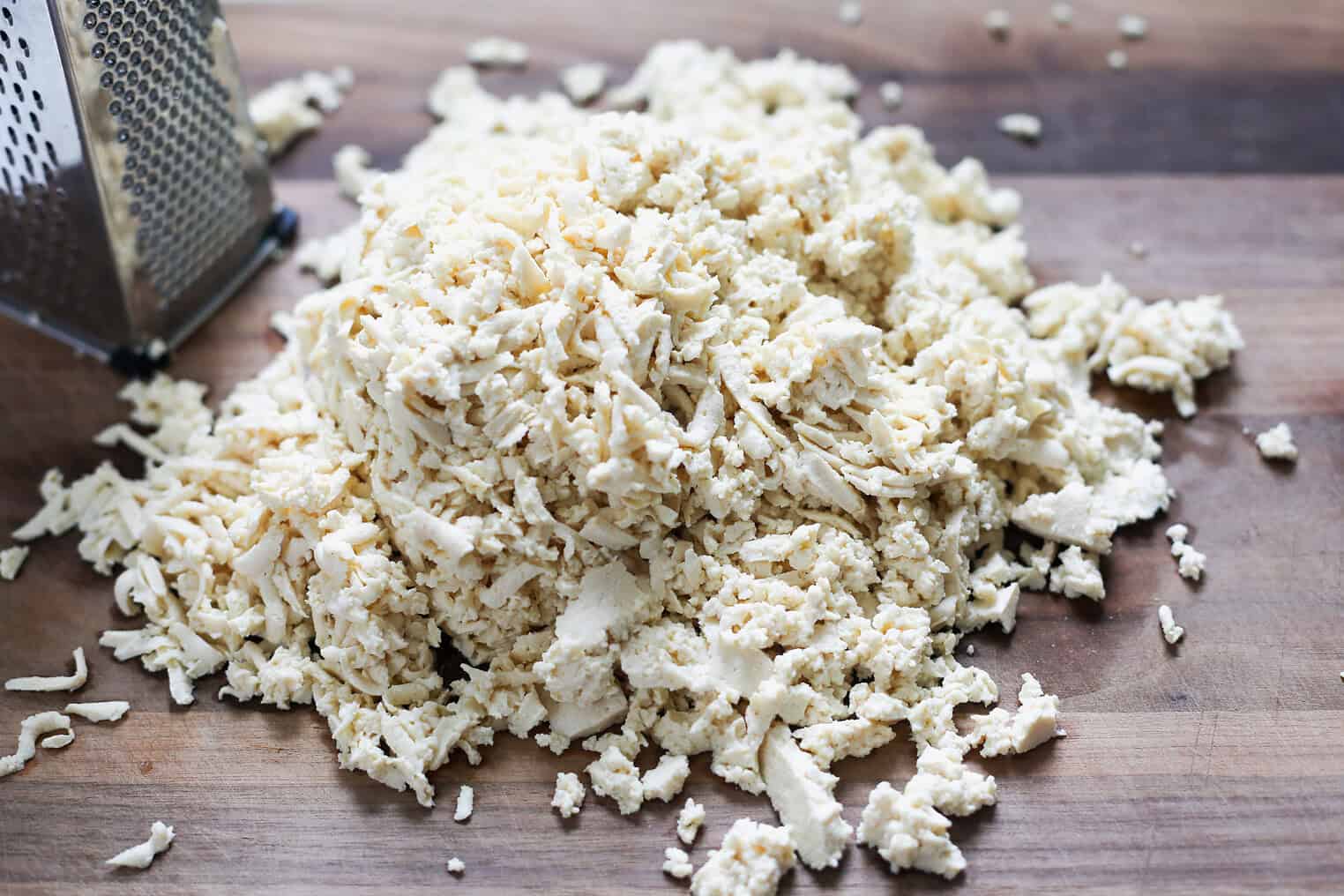 Vegan Thai Larb Lettuce Wraps 4 A Pile Of Freshly Grated Cheese Sits On A Wooden Surface Next To A Metal Box Grater, With Small Cheese Shreds Scattered Around—Perfect For Topping Vegan Thai Larb Or Other Flavorful Dishes.