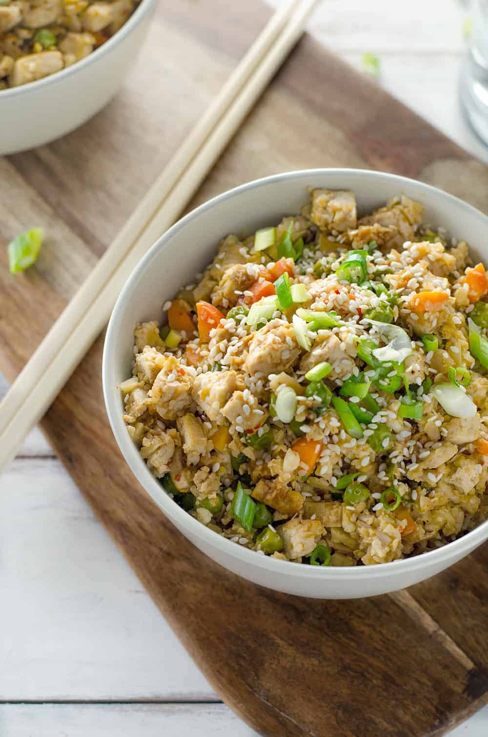 A Bowl Of Cauliflower Fried Rice With Carrots, Green Onions, And Peas 