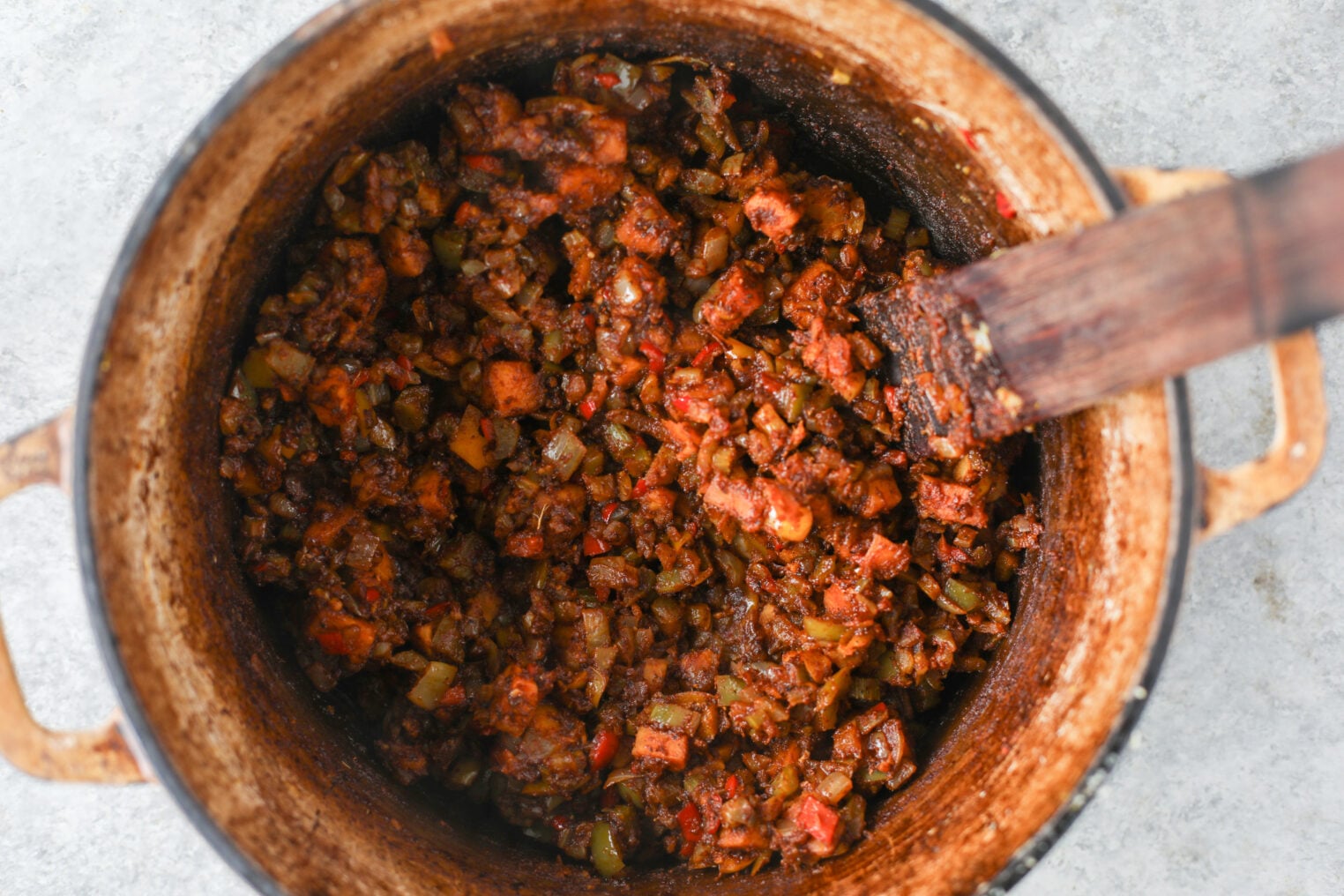 A Wooden Spoon Stirs A Dark, Chunky Vegetarian Chili Cooking In A Pot.