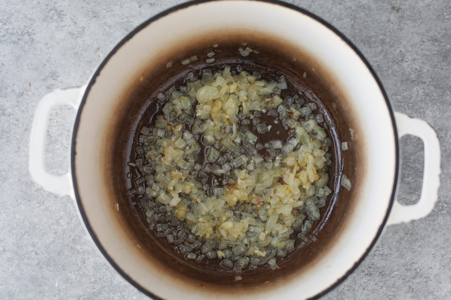 Chopped Onions Sautéing In A White Enamel Pot, Browning At The Edges, Are The Perfect Start For A Hearty Bean Orzo Soup, All Set On A Gray Countertop.