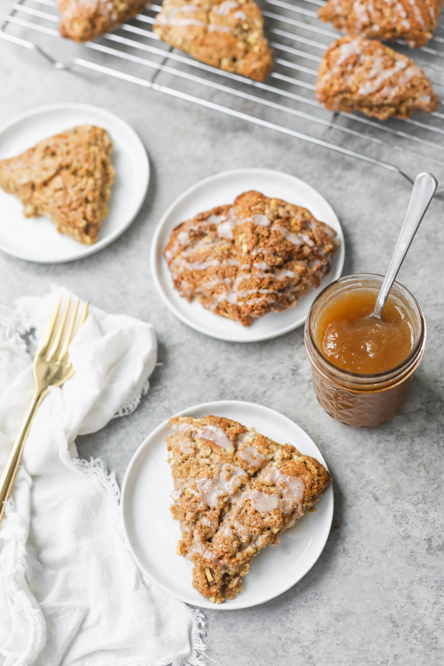 Whole Wheat Apple Scones 10 Three Plates With Triangle Apple Scones, A Jar Of Jam With A Spoon, And A Cooling Rack With More Scones In The Background. A White Napkin And Two Gold Forks Are On The Left.