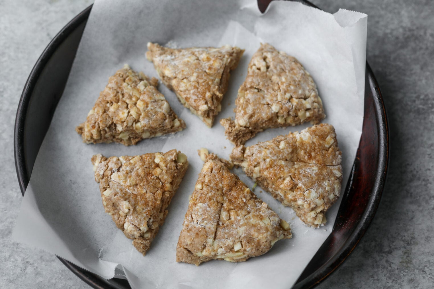 Whole Wheat Apple Scones 9 Six Unbaked, Triangular Apple Scones With A Crumbly Texture Are Arranged In A Circle On Parchment Paper In A Dark Baking Dish, Ready To Be Baked.