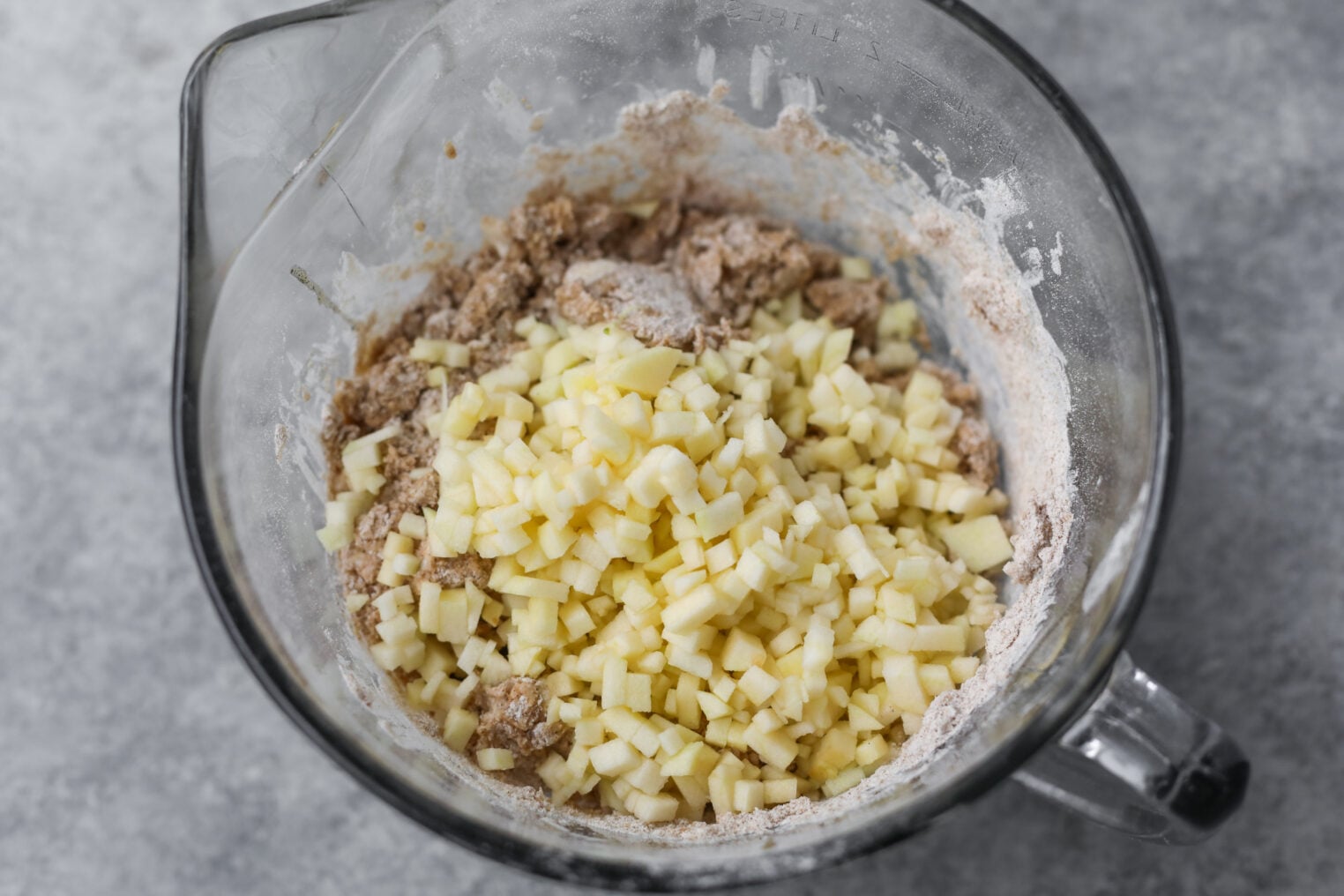 Whole Wheat Apple Scones 7 Overhead View Of A Glass Mixing Bowl Containing Flour, Chopped Apples, And Partially Mixed Dough On A Gray Surface—Perfect For Making Delicious Apple Scones.