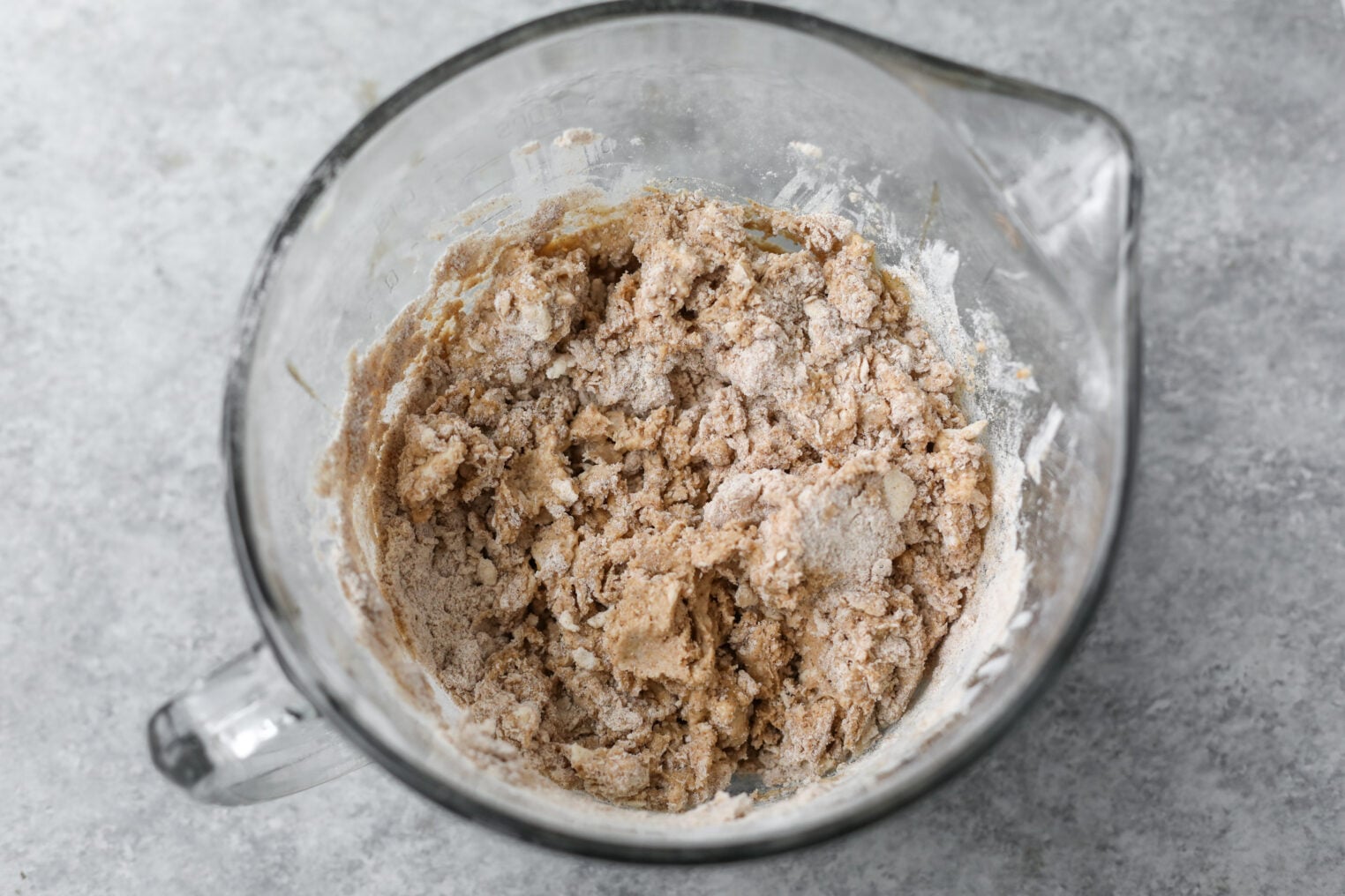 Whole Wheat Apple Scones 6 A Glass Mixing Bowl Filled With Partially Mixed, Light Brown Apple Scones Dough, With Some Flour Still Visible, Sits On A Gray Countertop.