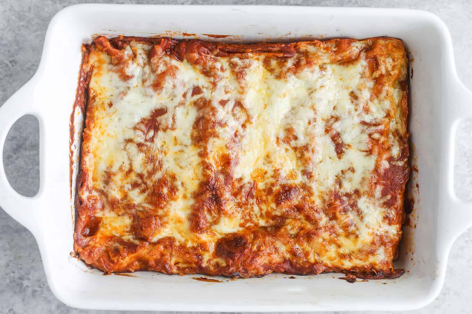 Bean and Cheese Enchiladas 9 A Baked Lasagna In A White Rectangular Dish, Topped With Melted Golden-Brown Cheese And Tomato Sauce, Reminiscent Of The Comforting Layers Found In Bean And Cheese Enchiladas.