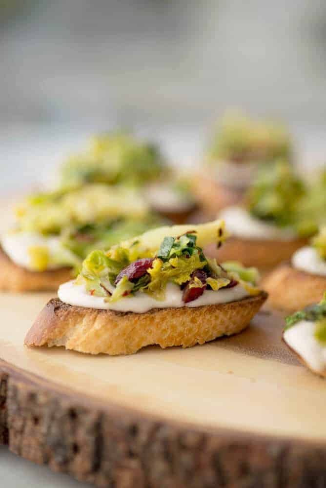 Vegan Brussels Sprout Crostini! Lemon-White Bean Spread topped with charred brussels sprouts and dried cranberry salad. A must-make for the holidays! | www.delishknowledge.com