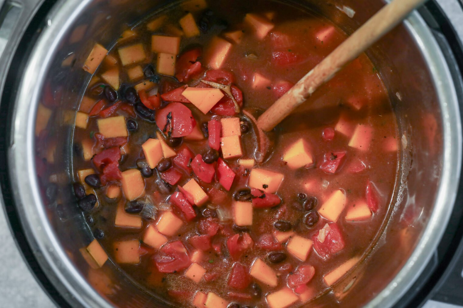 Slow Cooker Black Bean Chili with Butternut Squash 4 A Pot Of Slow Cooker Black Bean Chili Simmers With Diced Sweet Potatoes And Tomatoes In Savory Broth, Being Stirred With A Wooden Spoon.