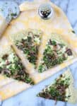 The best dairy-free pizza! Herb and garlic crust topped with creamy white sauce, caramelized onions, fresh herbs and vegan parm sprinkle.