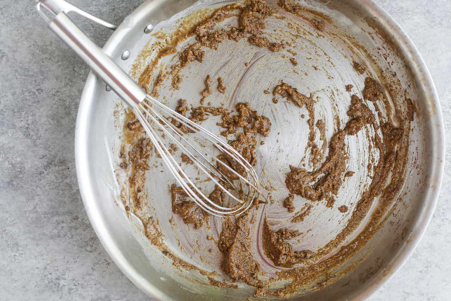 Homemade Enchilada Sauce 7 A Metal Whisk Rests In A Stainless Steel Pan With Remnants Of A Brown, Thick Easy Homemade Enchilada Sauce Swirled Across The Bottom, Sitting On A Light Gray Countertop.