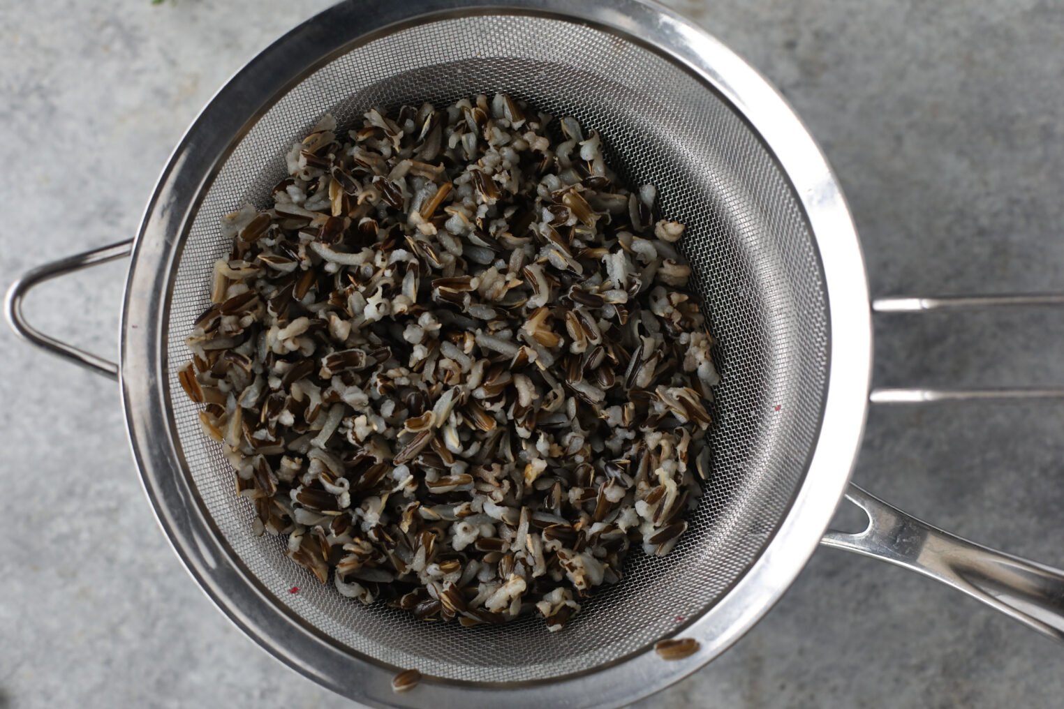A Metal Strainer With Cooked Wild Rice Draining Over A Gray Countertop, Viewed From Above—Perfectly Prepped For A Fresh Wild Rice And Kale Salad.