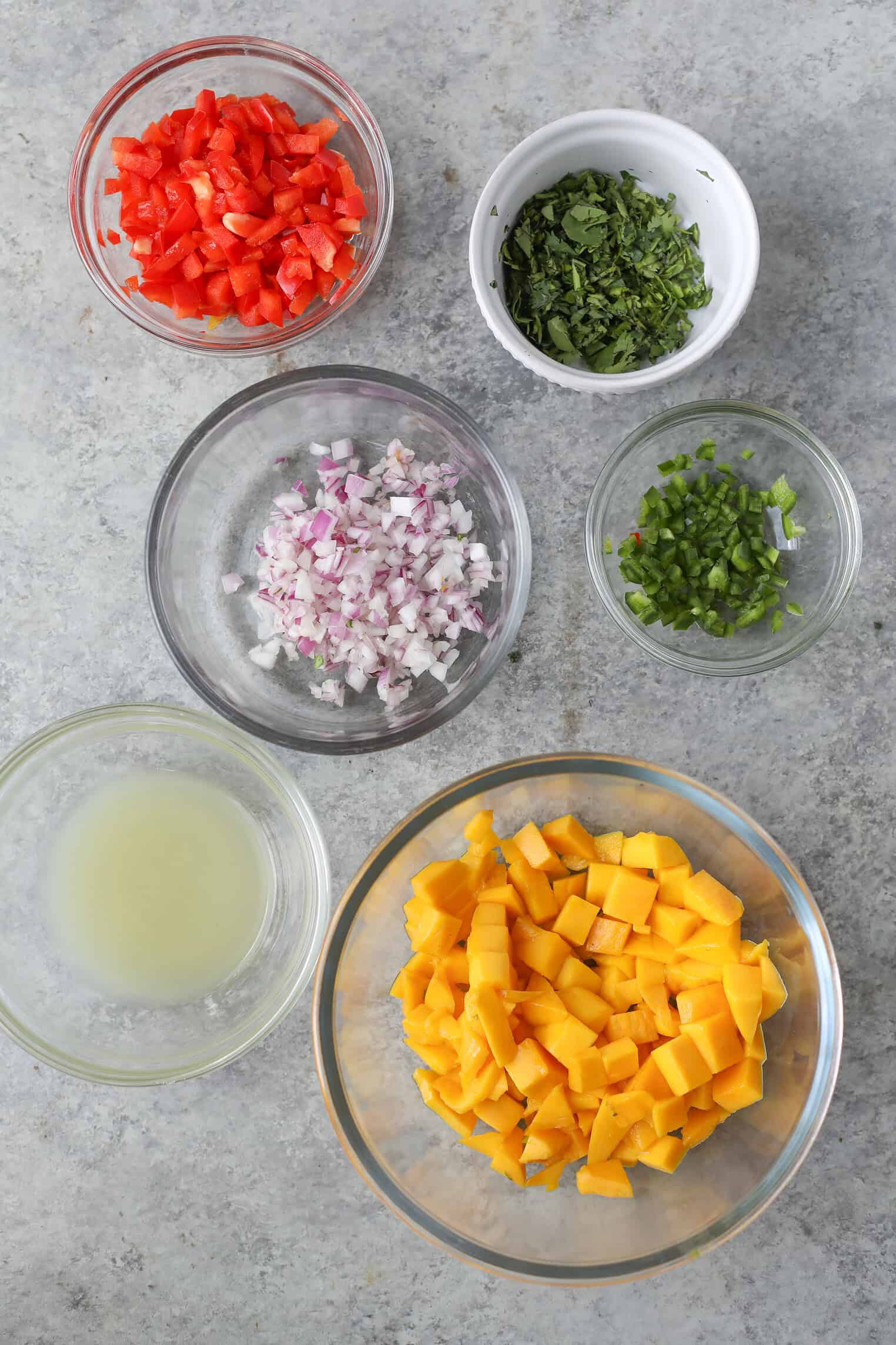 Six Mango Salsa Bowls Sit On A Gray Surface, Each Filled With Diced Red Bell Pepper, Chopped Fresh Herbs, Red Onion, Green Onions, Lime Juice, And Juicy Diced Mango.