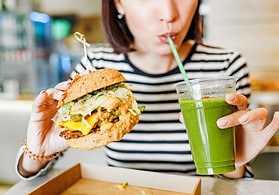 A young woman drinks green smoothies and eats a burger in a vegan fast food restaurant