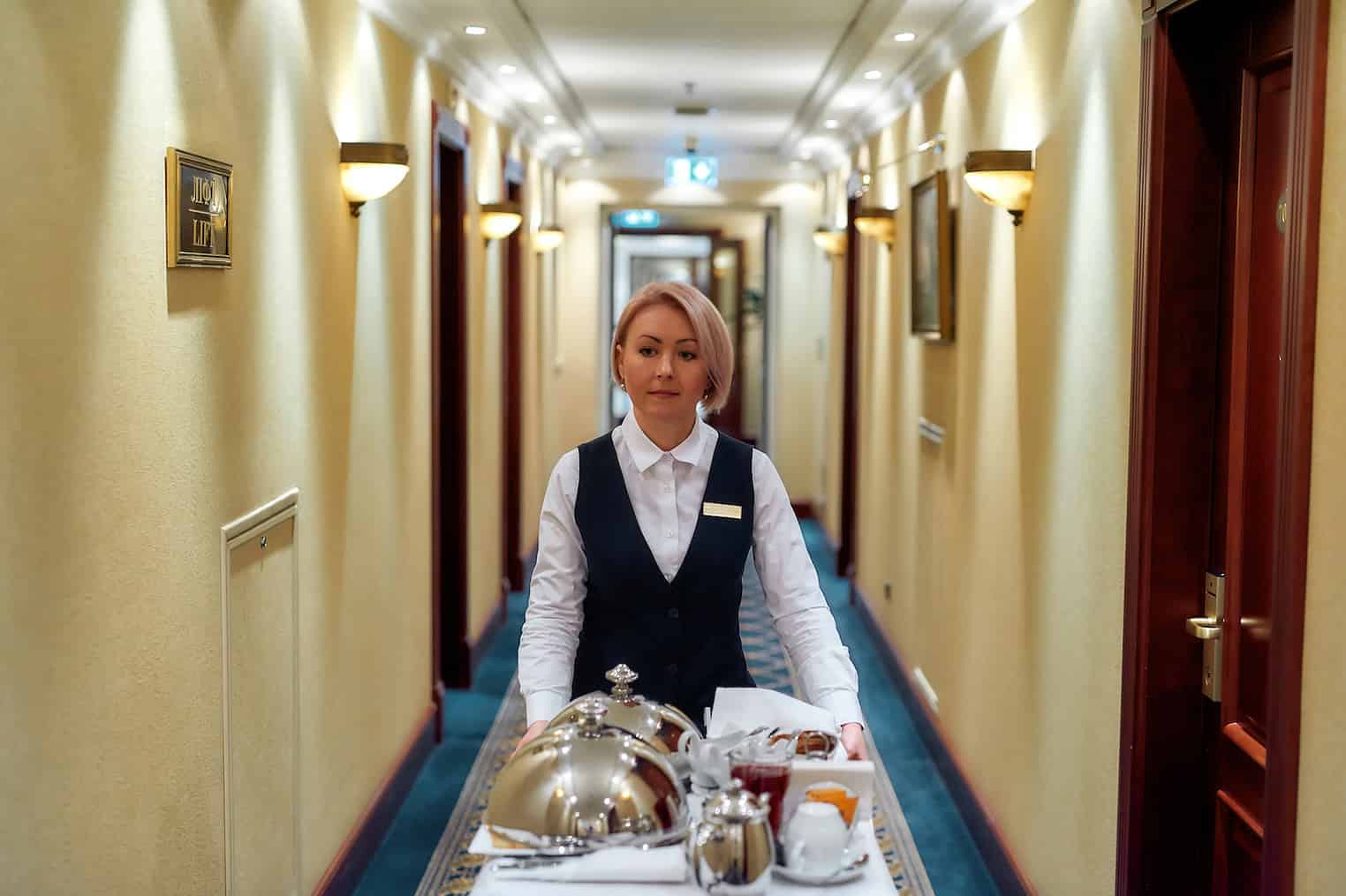 8 Features Every Family Should Look for in an All-Inclusive Resort 6 Waitress In Uniform Walking Along The Hall While Delivering Tray With Food In A Room Of Hotel. Room Service. Horizontal Shot. Front View
