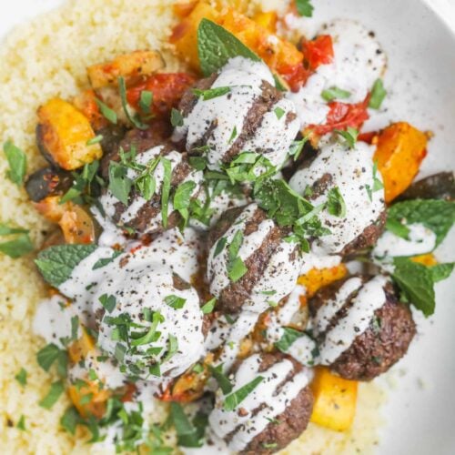 Vegan Kofta Plates with Roasted Vegetables and Couscous 13 A Plate Of Couscous Topped With Roasted Vegetables And Beef Meatballs, All Drizzled With Yogurt Sauce. Garnished With Chopped Parsley And Mint Leaves For A Fresh Finish, This Dish Offers An Inviting Twist Reminiscent Of Vegan Kofta'S Delightful Flavors.