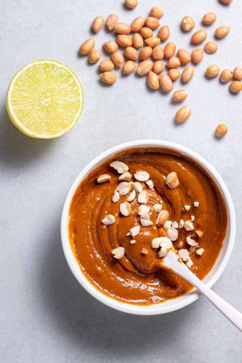 Spicy lime peanut sauce for Vietnamese spring rolls in white bowl with spoon and lime