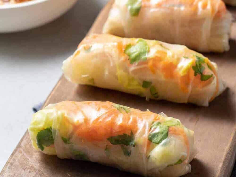 four Vietnamese spring rolls on wooden tray with spicy peanut sauce in bowl
