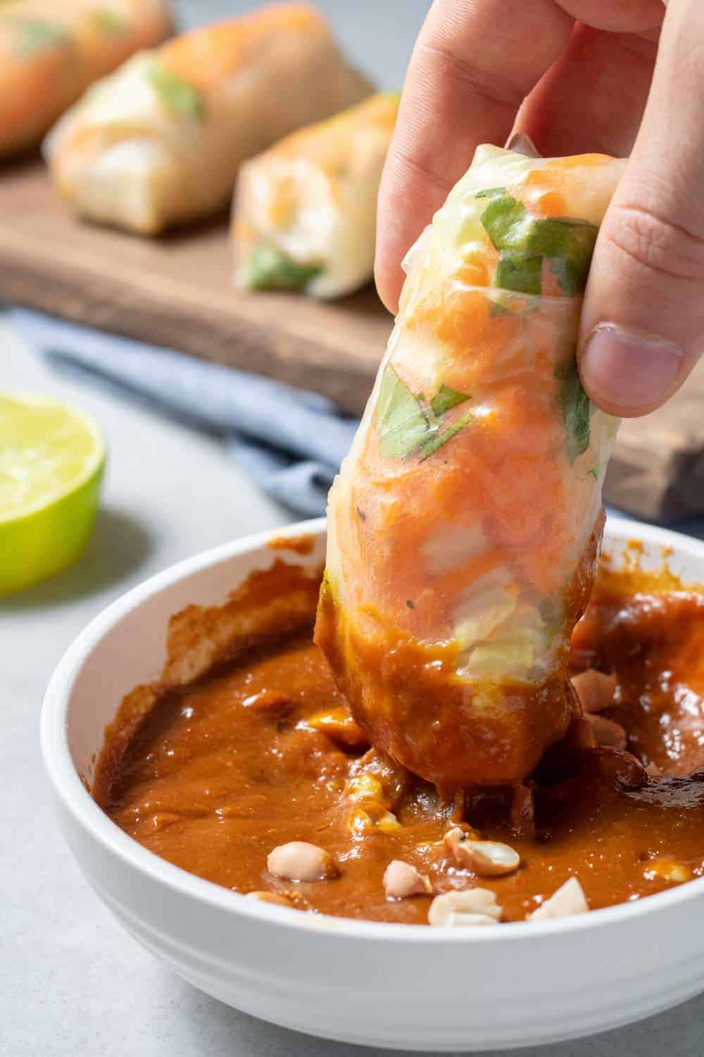 Dipping Spring Rolls Into Peanut Sauce In A White Bowl